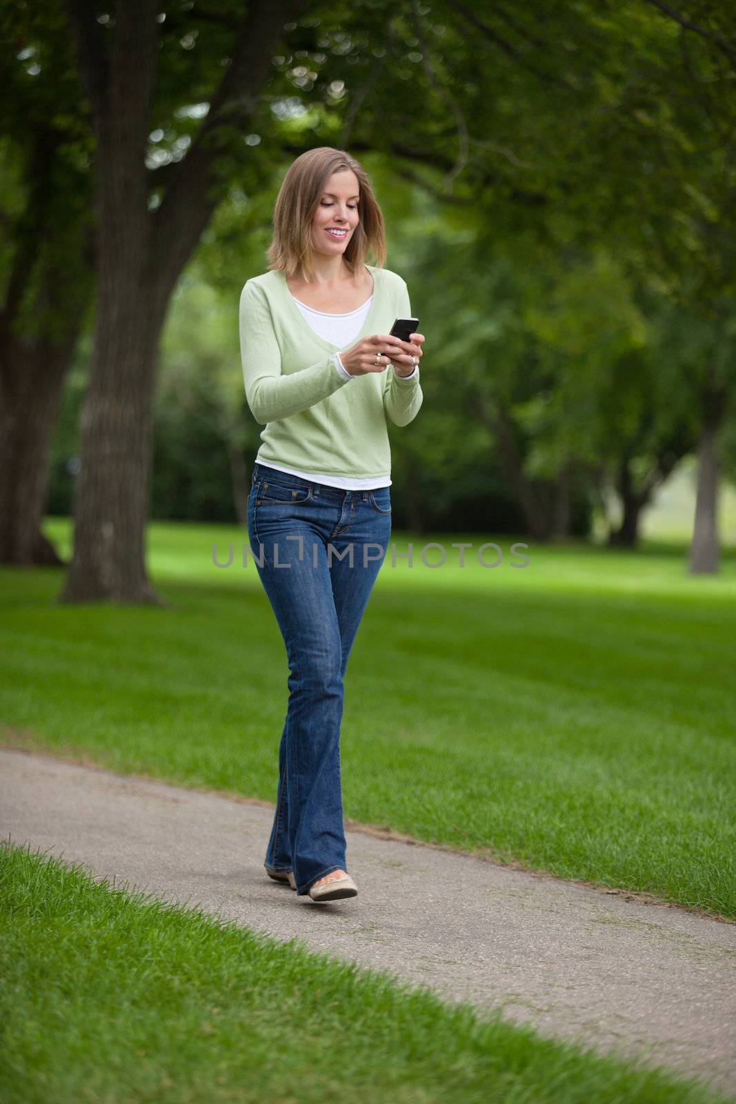 Full length of a young woman text messaging as she walks in park
