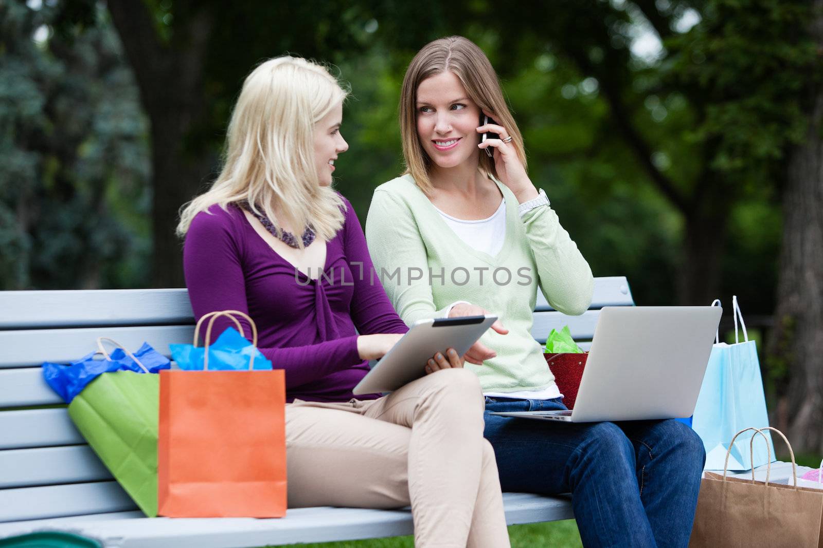 Shopping Women Using Digital Tablet, computer and cellphone on bench.