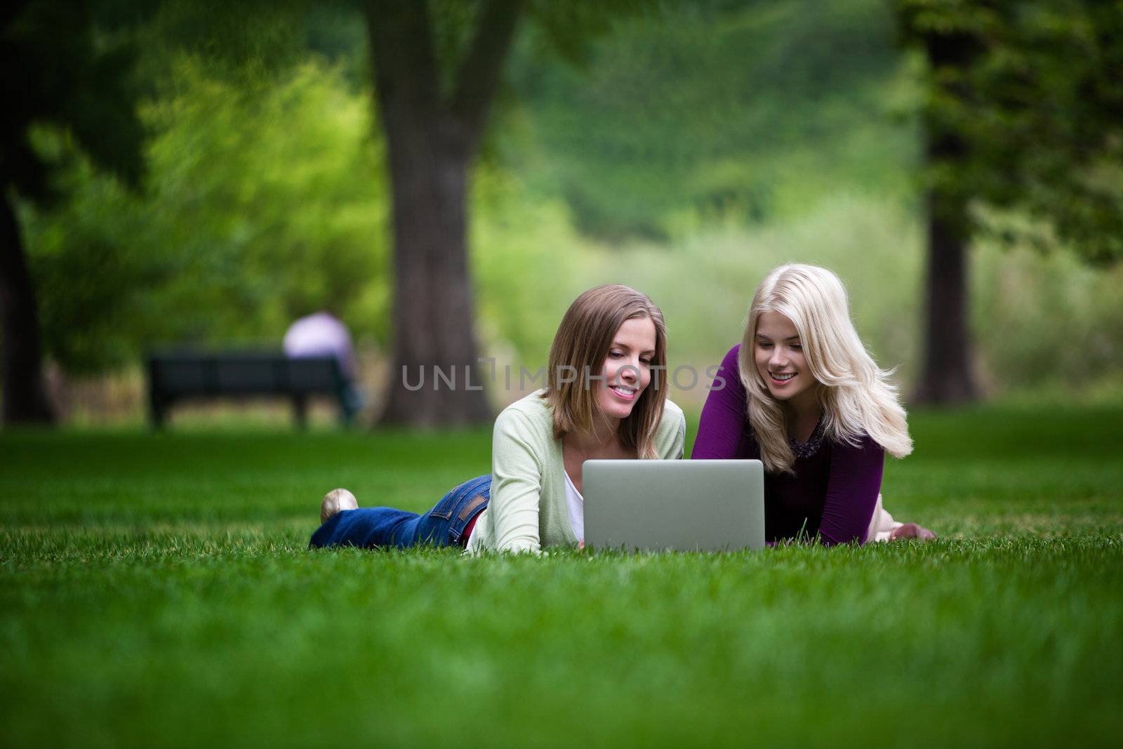 Two young happy women using laptop in park