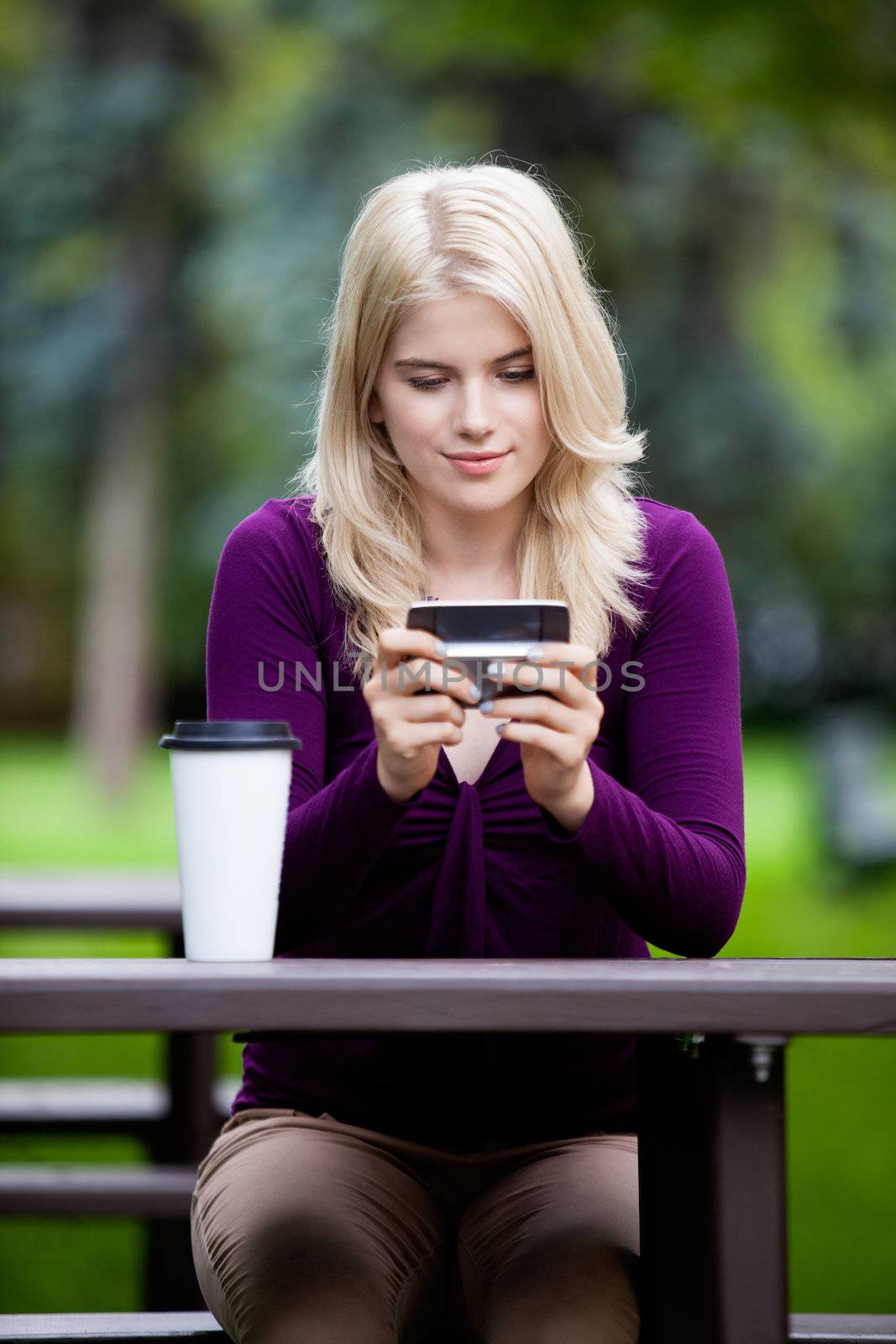 Happy blond woman sitting at park bench using cell phone