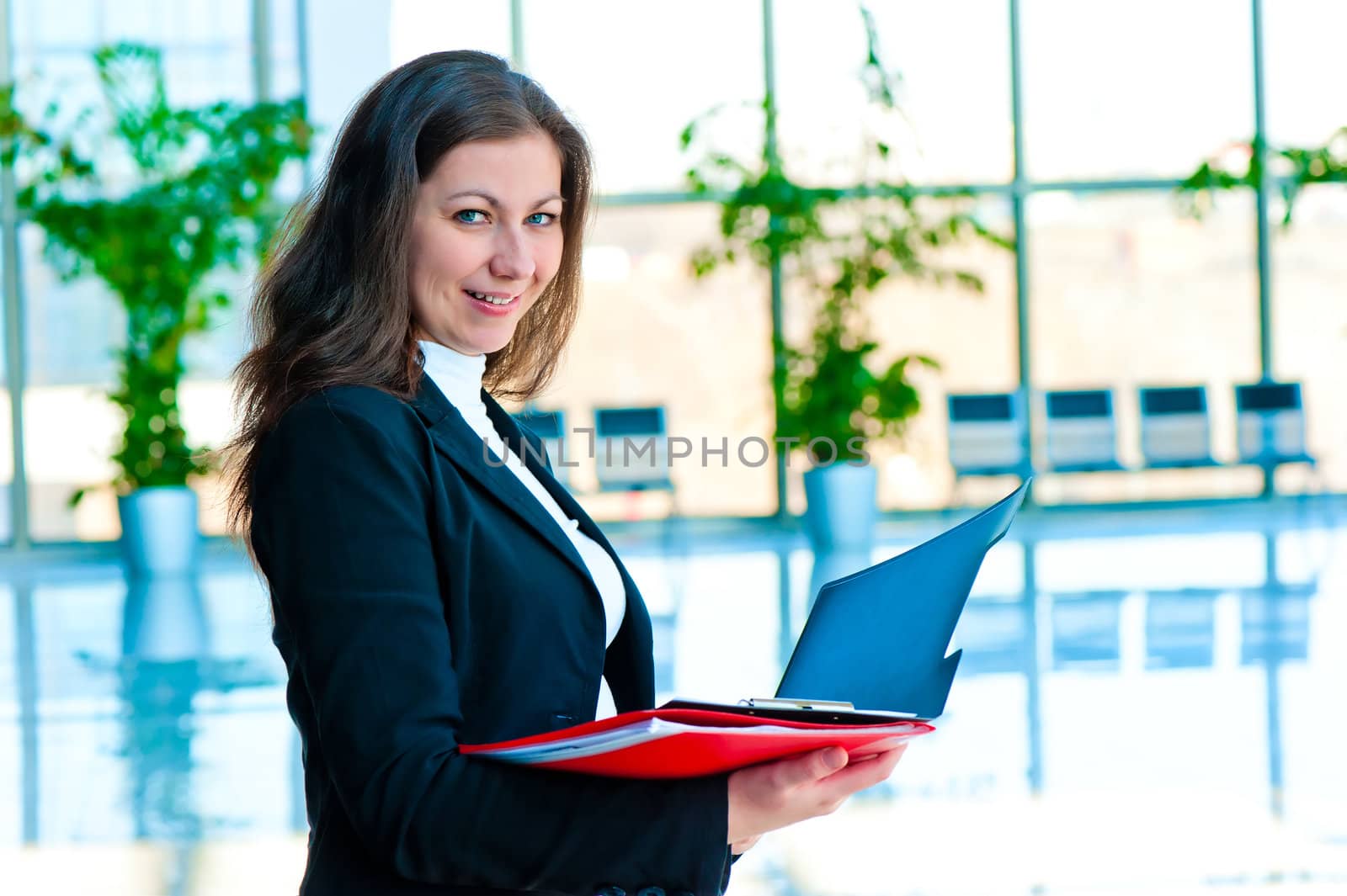 Happy businesswoman holding an open folders on the background of office interior by kosmsos111
