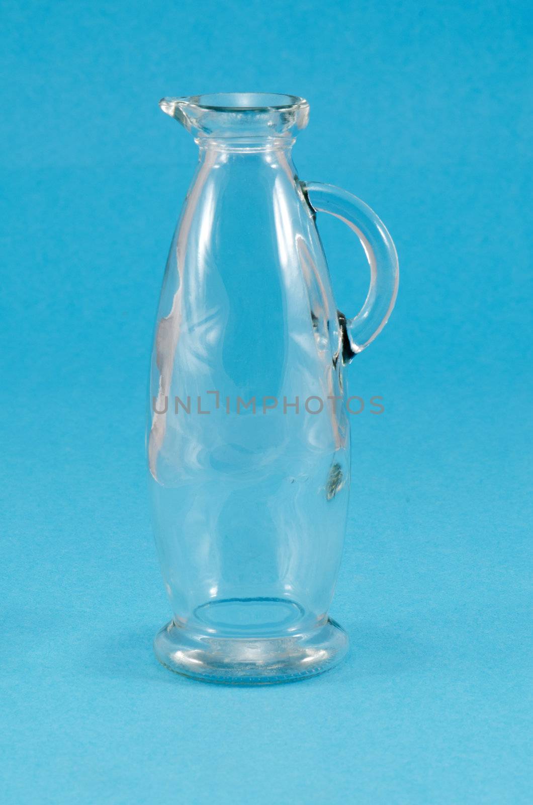 old transparent empty glass jug jar with handle on blue background.