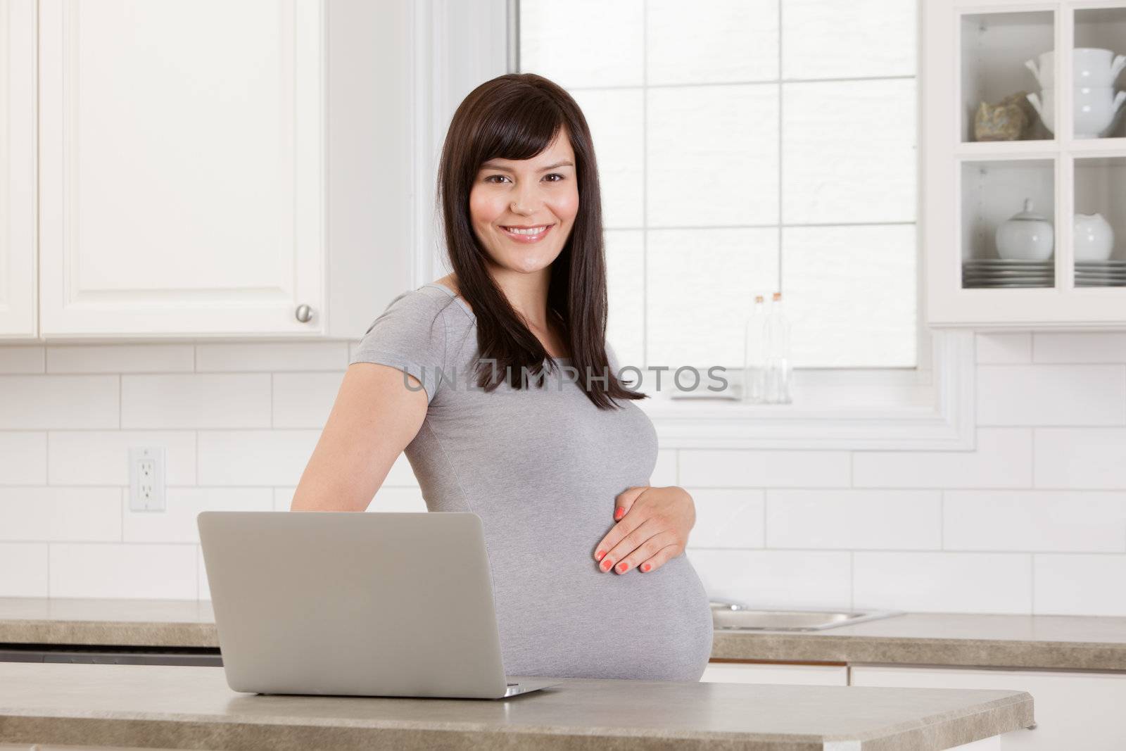 Happy healthy pregnant woman in kitchen with laptop computer