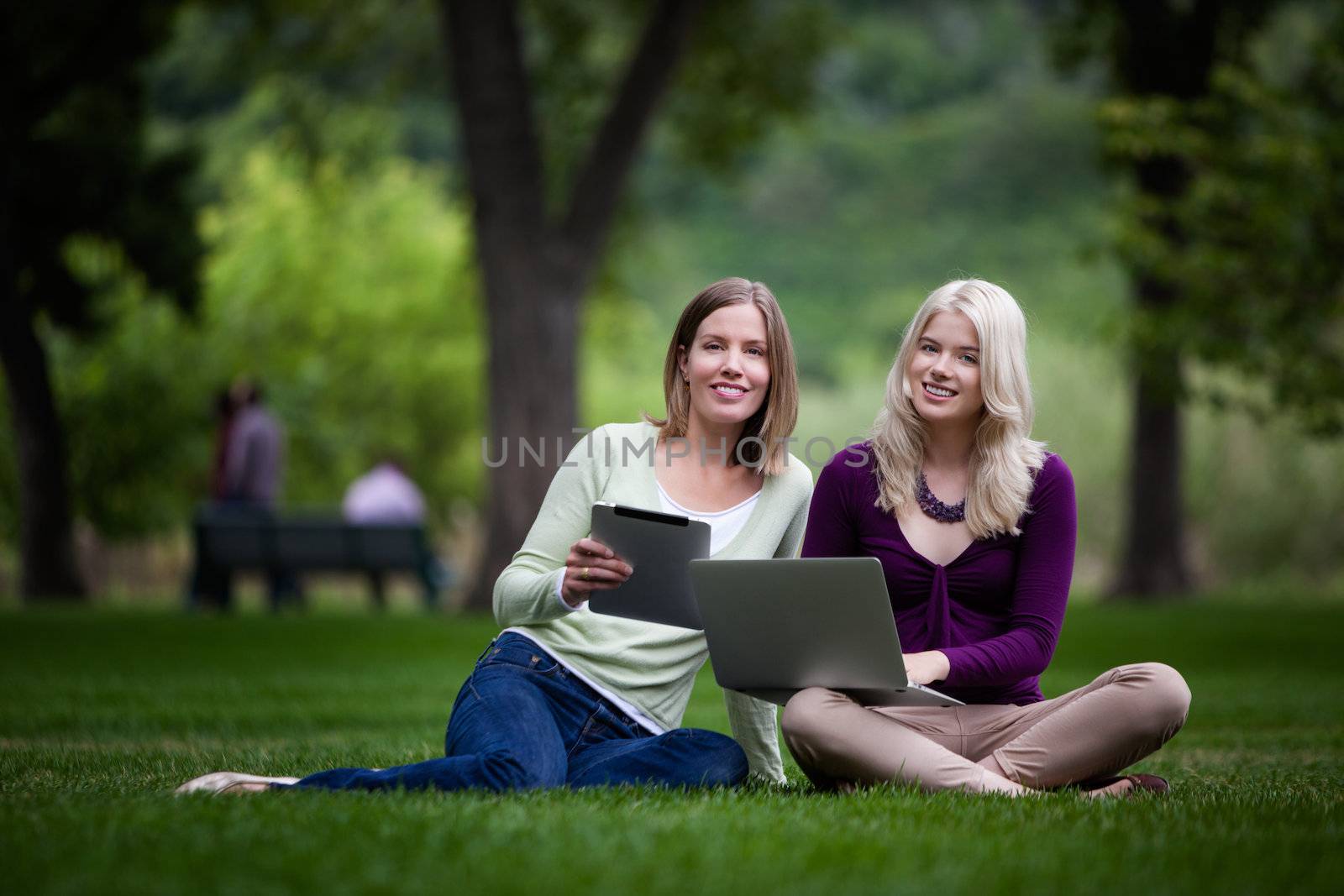 Smiling young women looknig at camera with computer and digital tablet in hand