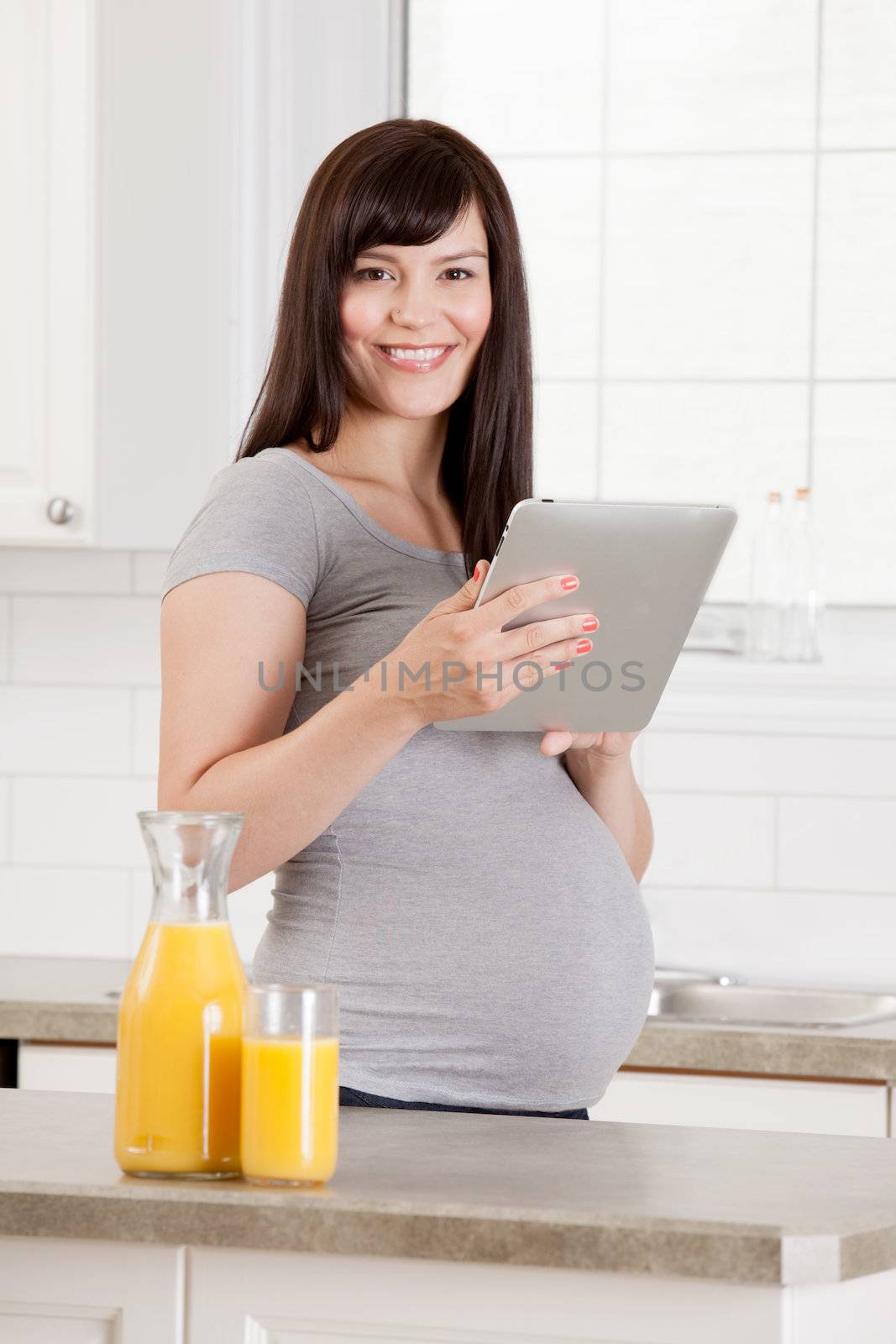 Pregnant woman in kitchen with digital tablet and orange juice