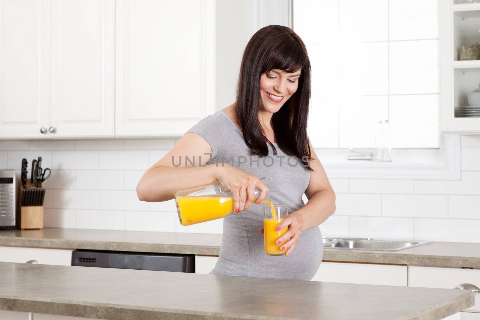 Pregnant woman pouring glass of orange juice in kitchen