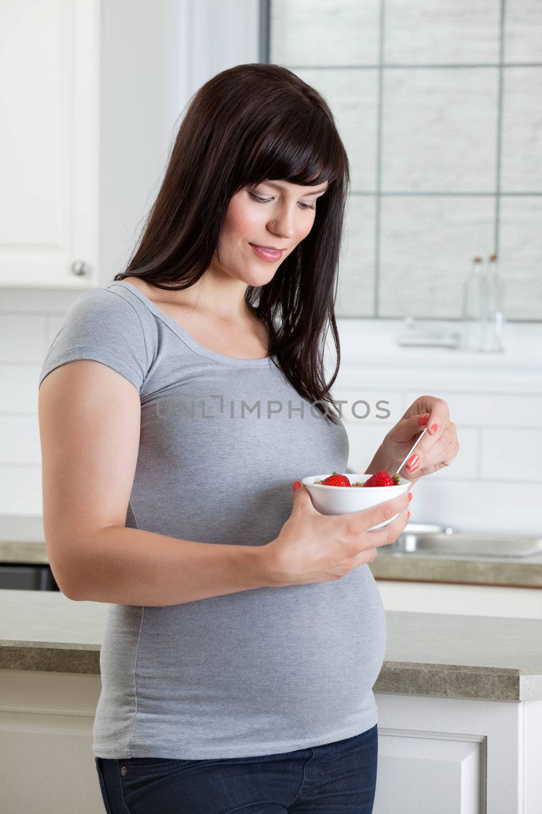Pregnant woman eating healthy bowl of fruit in kitchen