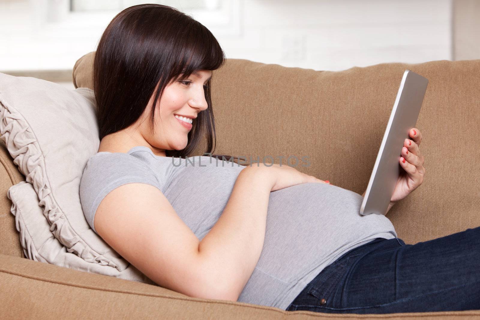 Happy pregnant woman sitting on sofa looking at a tablet computer