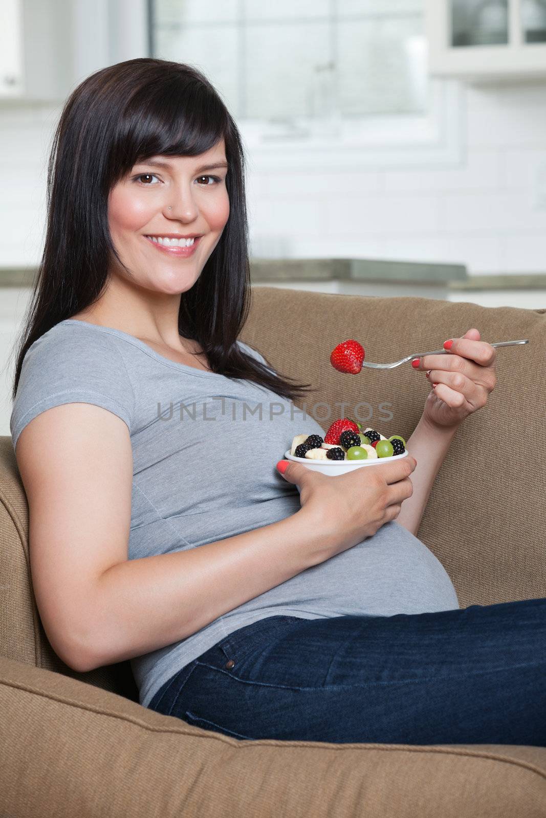 Portrait of pregnant woman eating fruit salad while sitting in sofa