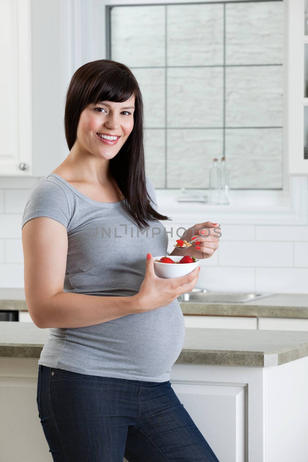Portrait of pregnant woman eating healthy bowl of fruit in kitchen