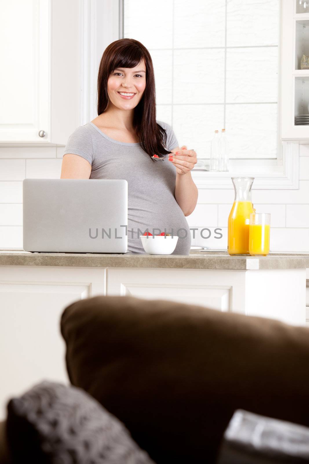 Happy smiling pregnant woman in kitchen eating breakfast in kitchen