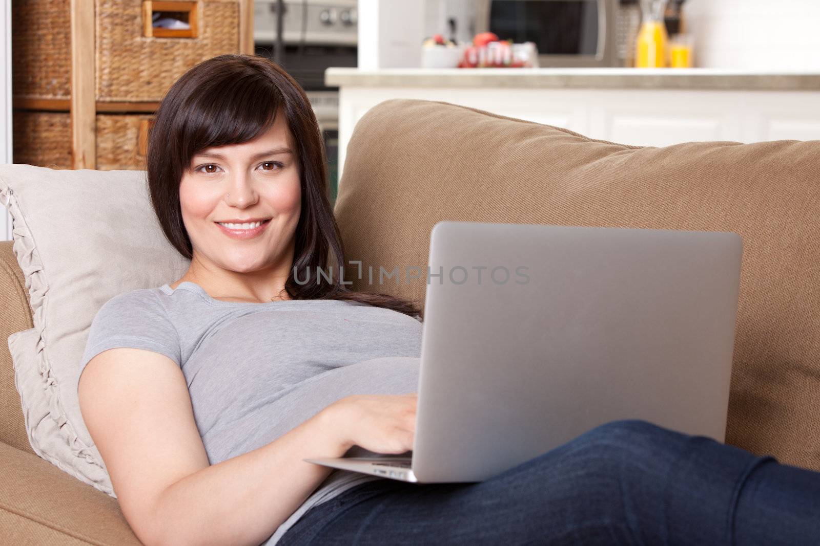 Happy pregnant woman looking at camera using laptop computer