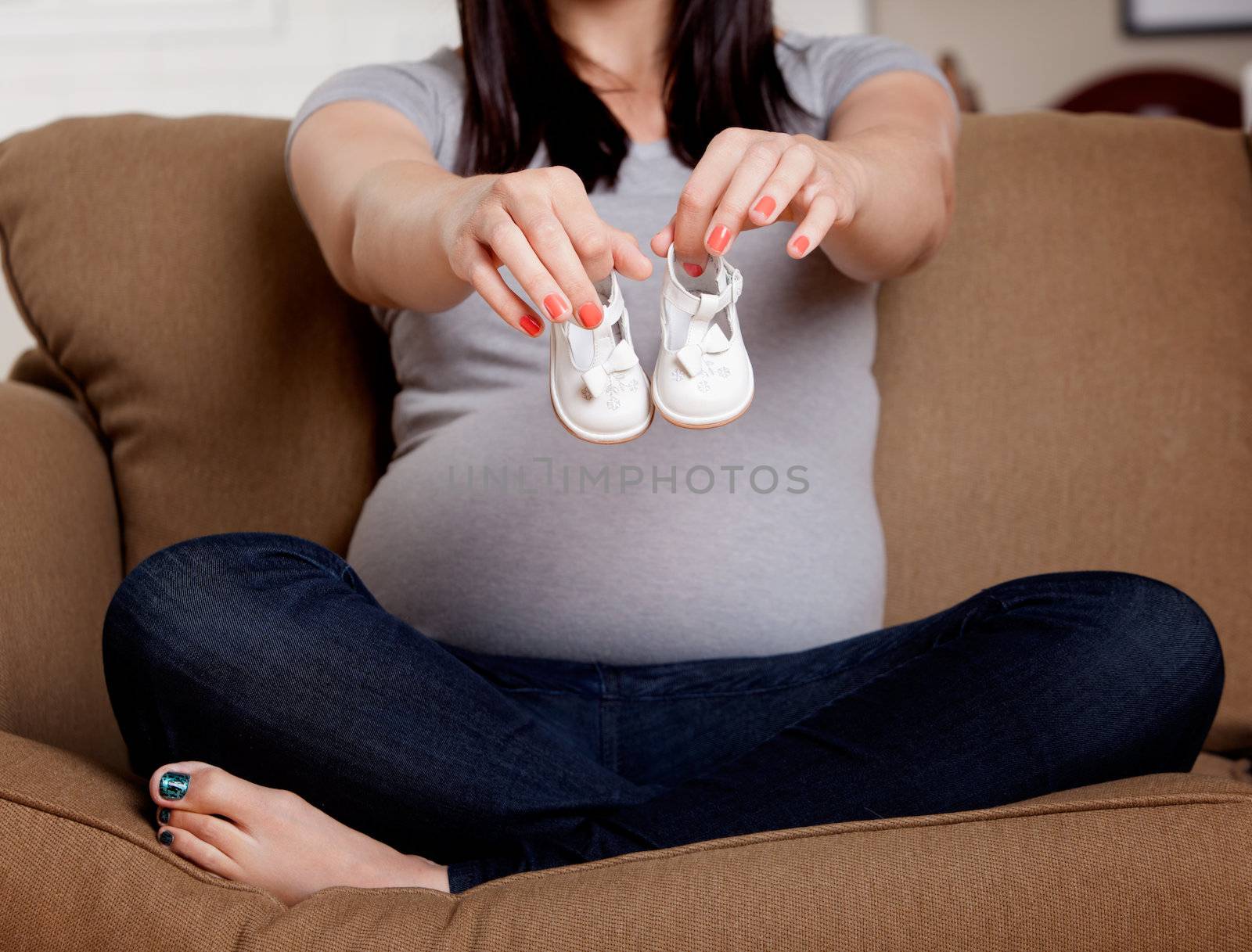 Young pregnant woman holding baby shoes in front of belly