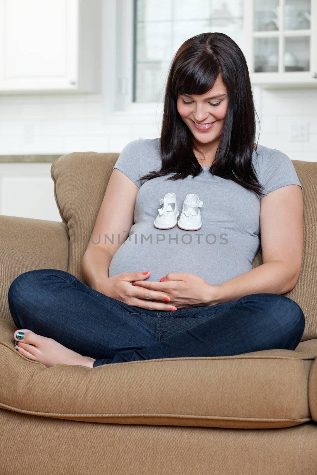 Pregnant Woman Looking At Baby Shoes On Her Belly by leaf
