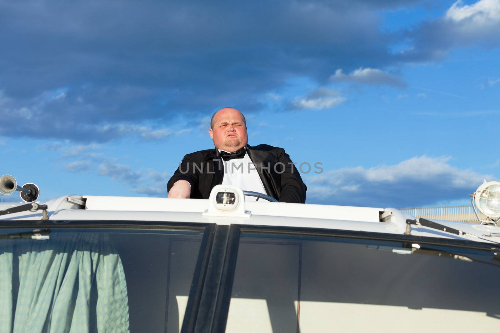 Overweight man in a tuxedo at the helm of a pleasure boat, closeup