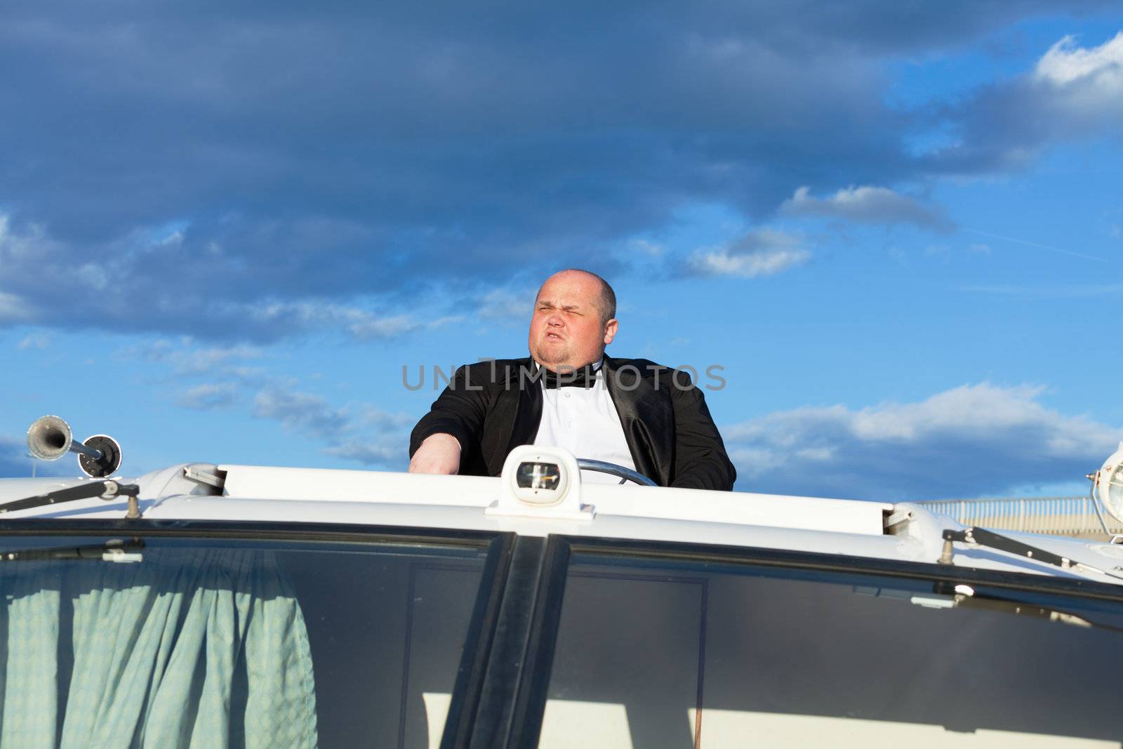 Overweight man in a tuxedo at the helm of a pleasure boat, closeup