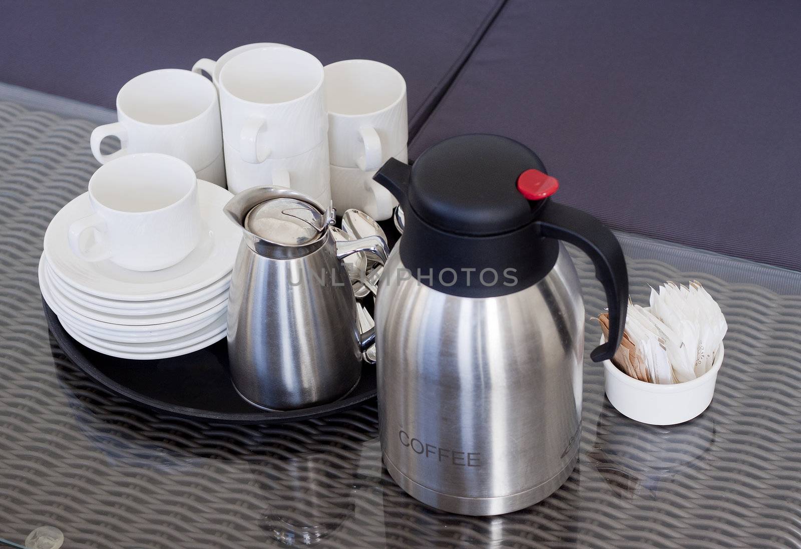 A rattan table with a tray of empty cups, saucers, coffee pot and sugar