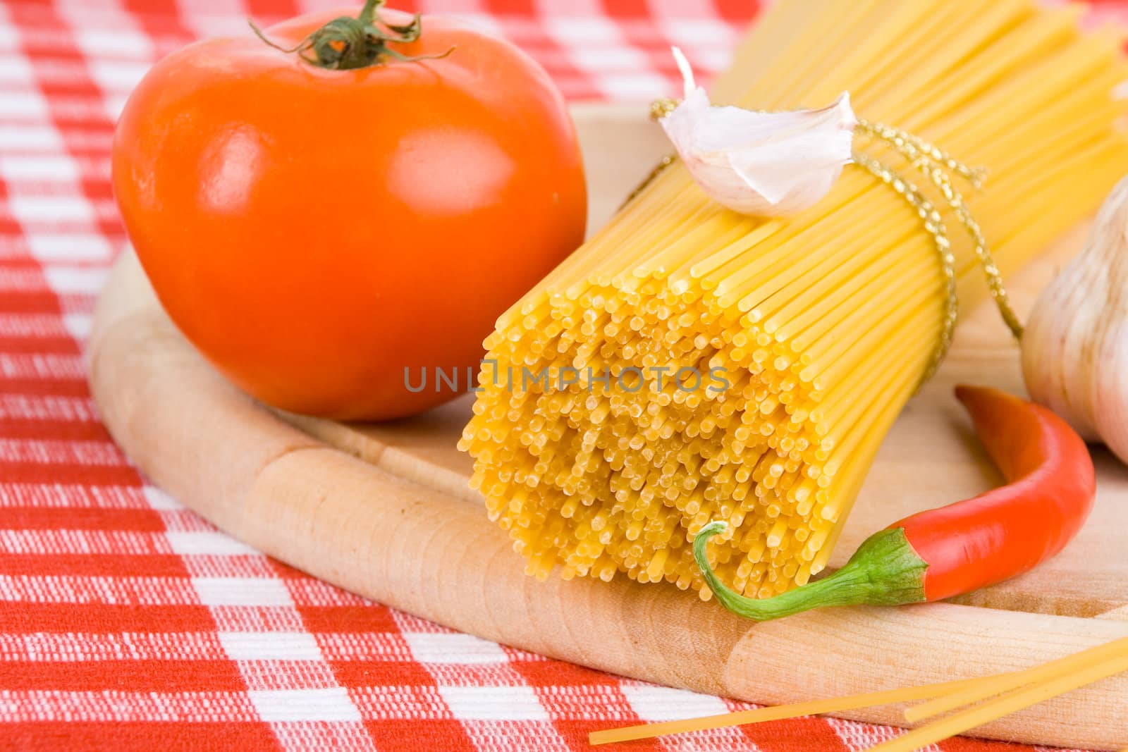 Golden raw dried Italian pasta with other ingredients on kitchen desk.