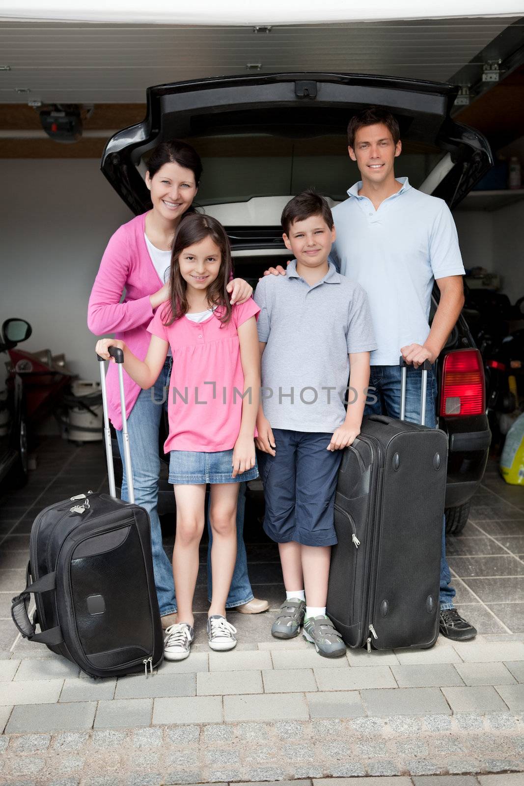 Happy family going on holiday standing by their car boot with their luggage