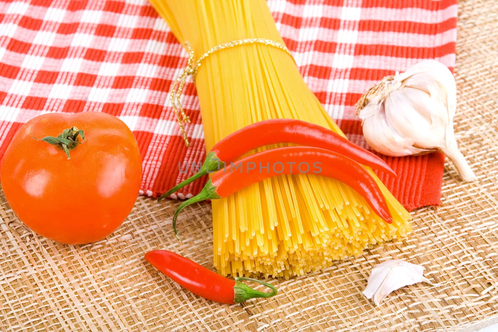 Golden raw dried Italian pasta with other ingredients on kitchen desk.