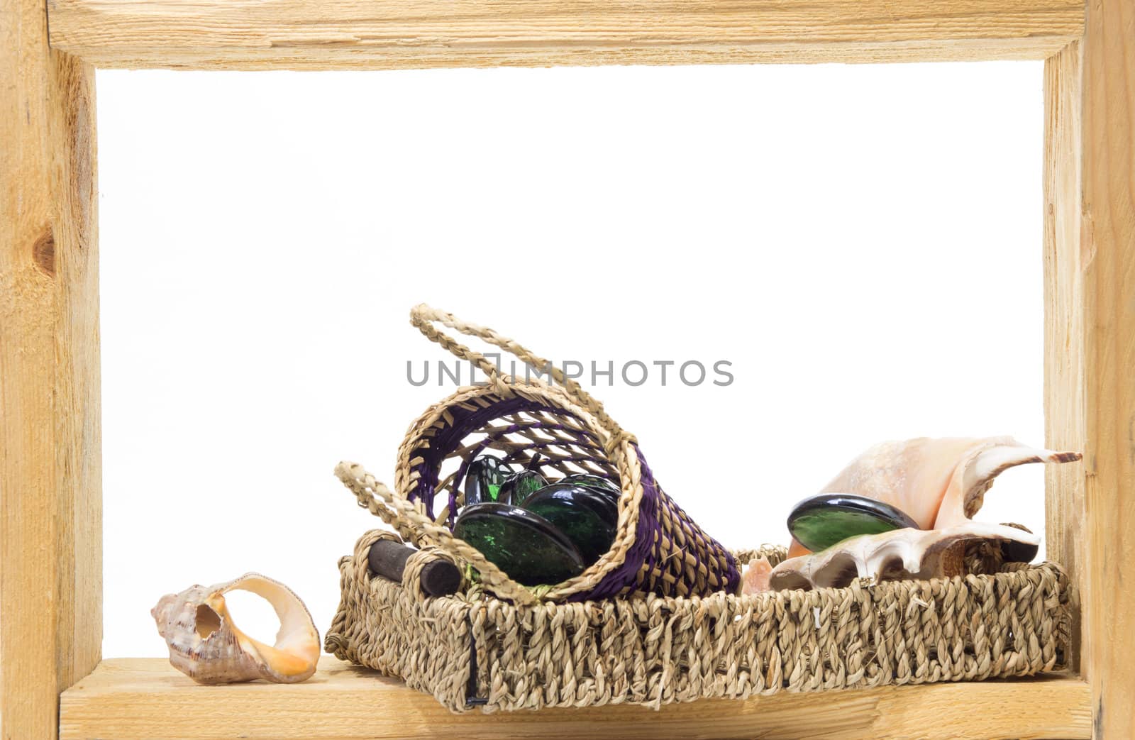 Wicker, green pieces of glass and sea shells inside rough wooden frame on white background