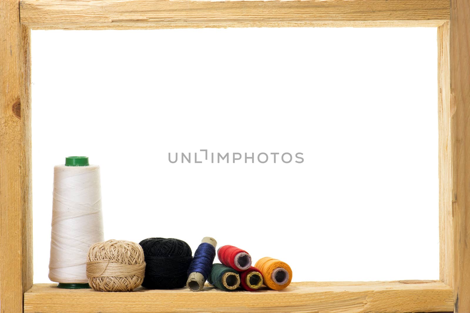 Spools with colored sewing thread inside rough wooden frame on white background 