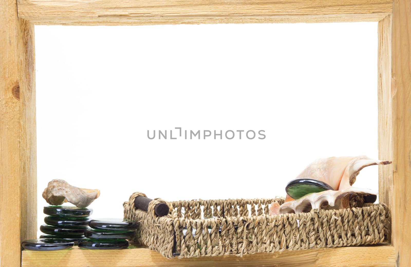 Wicker, green pieces of glass and sea shells inside rough wooden frame on white background