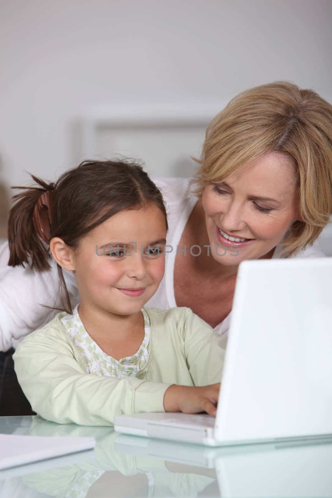 Mother and young daughter using a white laptop computer together by phovoir