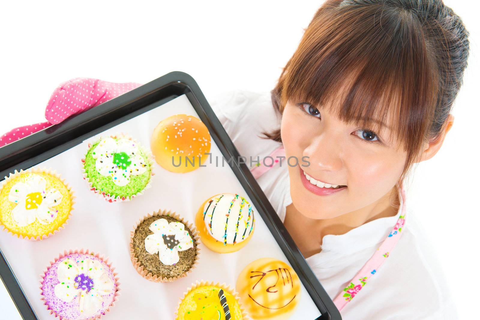 Young Asian woman baking bread and cupcakes, wearing apron and gloves holding tray isolated on white.
