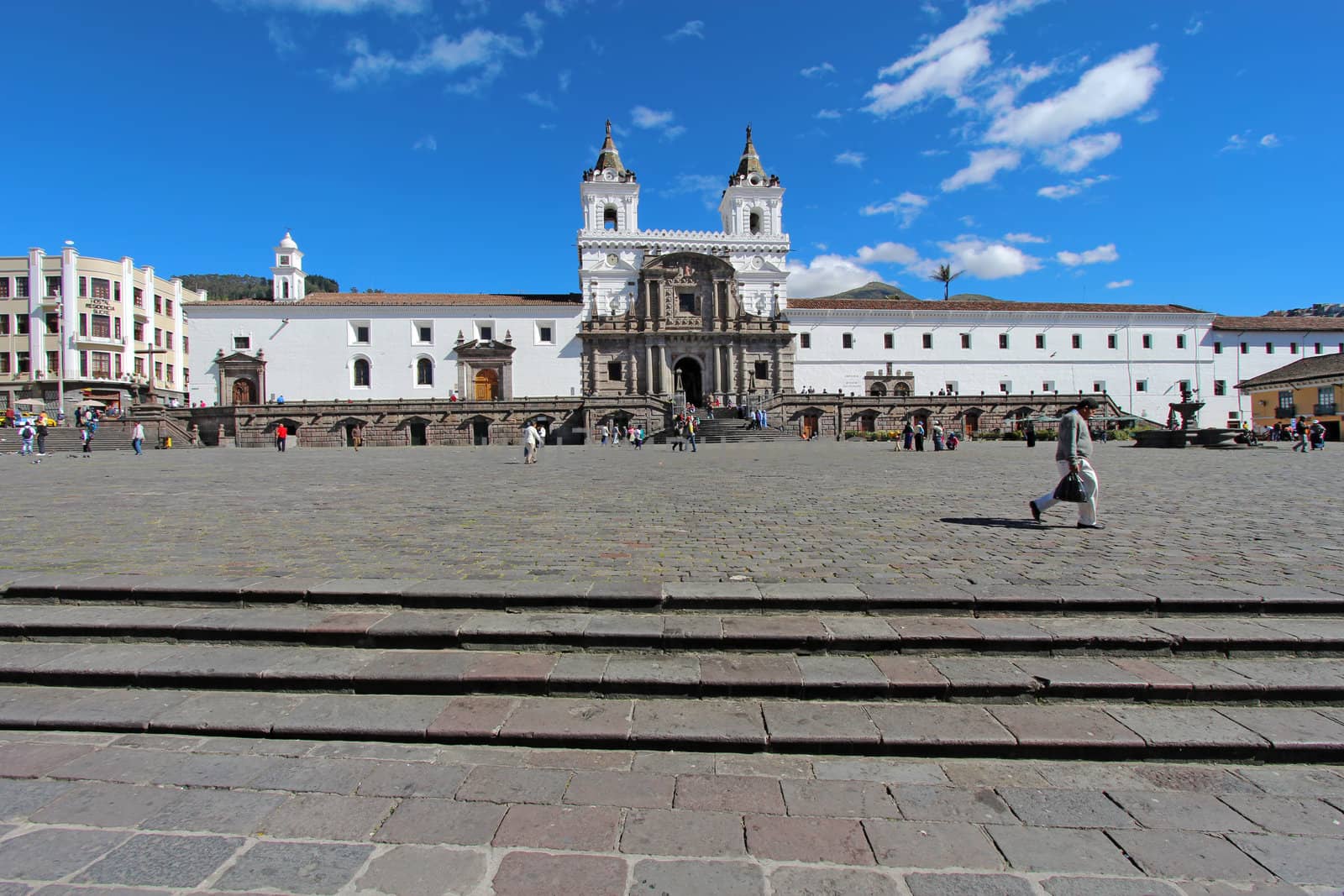 QUITO, ECUADOR - JUNE 1: People go about their business in the plaza in front of the church and convent of San Francisco in the historic part of downtown Quito, Ecuador against a bright blue sky and white clouds on June 1, 2012