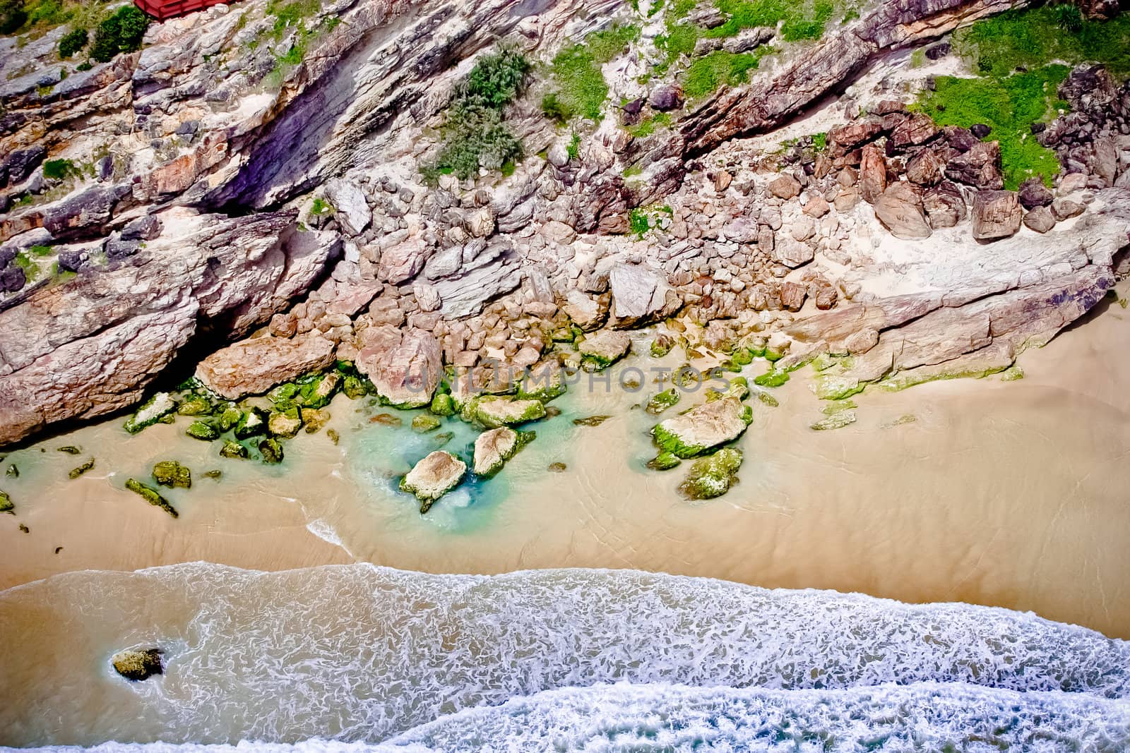 Aerial view of a pretty coastal bay with rocky cliffs and golden beach being lapped by gentle surf