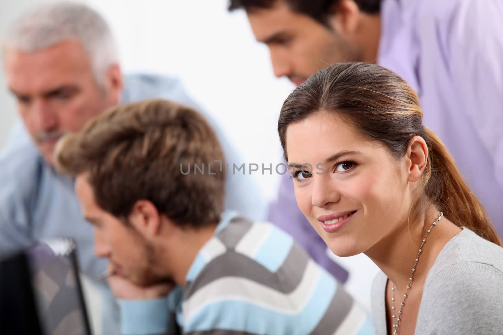Smiling young woman with male colleagues out of focus in the background by phovoir