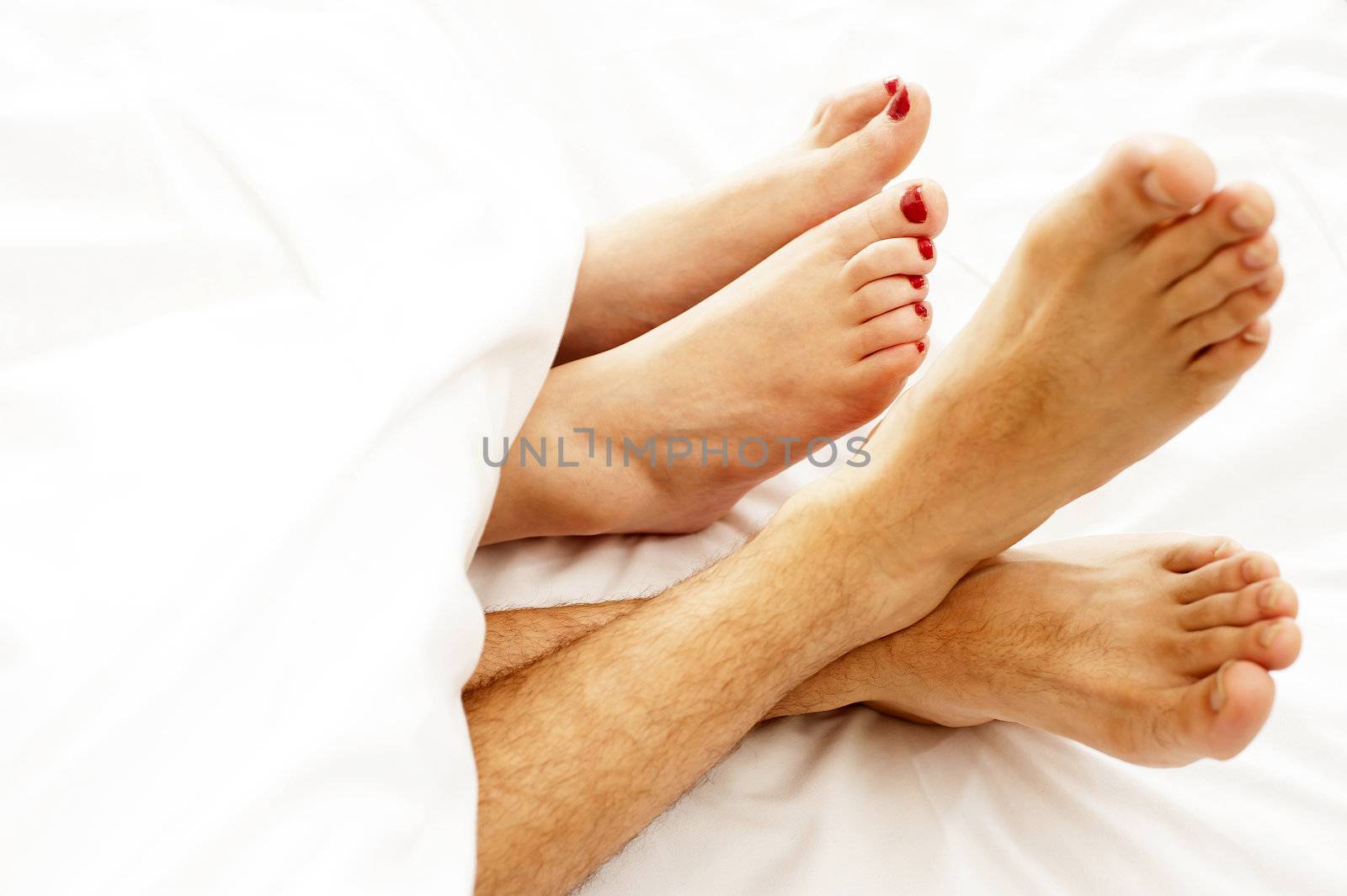 Closeup of bare feet of love couple, making out. Covered with white sheets