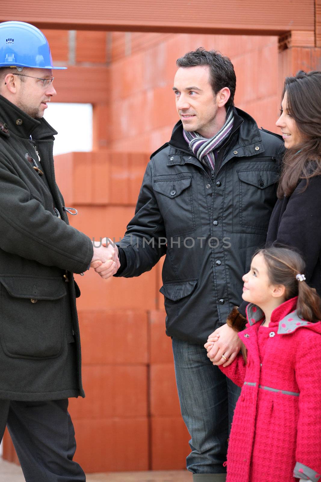 Architect shaking hands with a young family on site