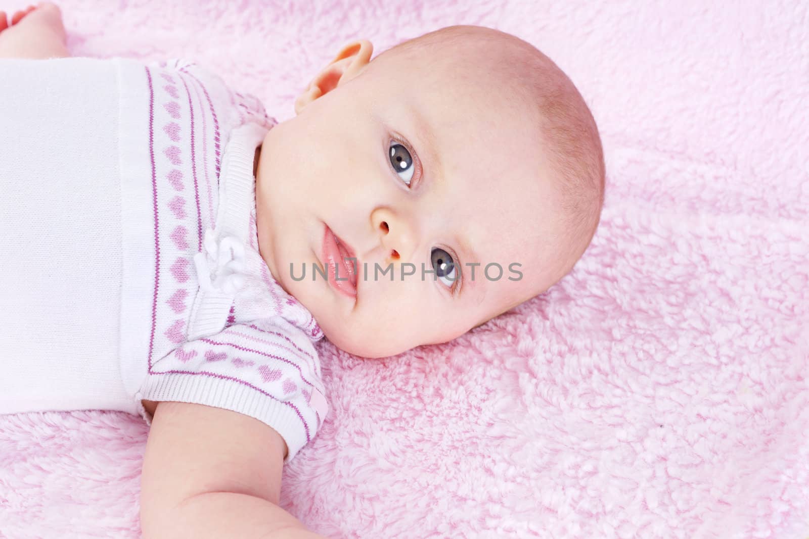 Portrait of newborn baby girl looking at camera, laying on pink blanket