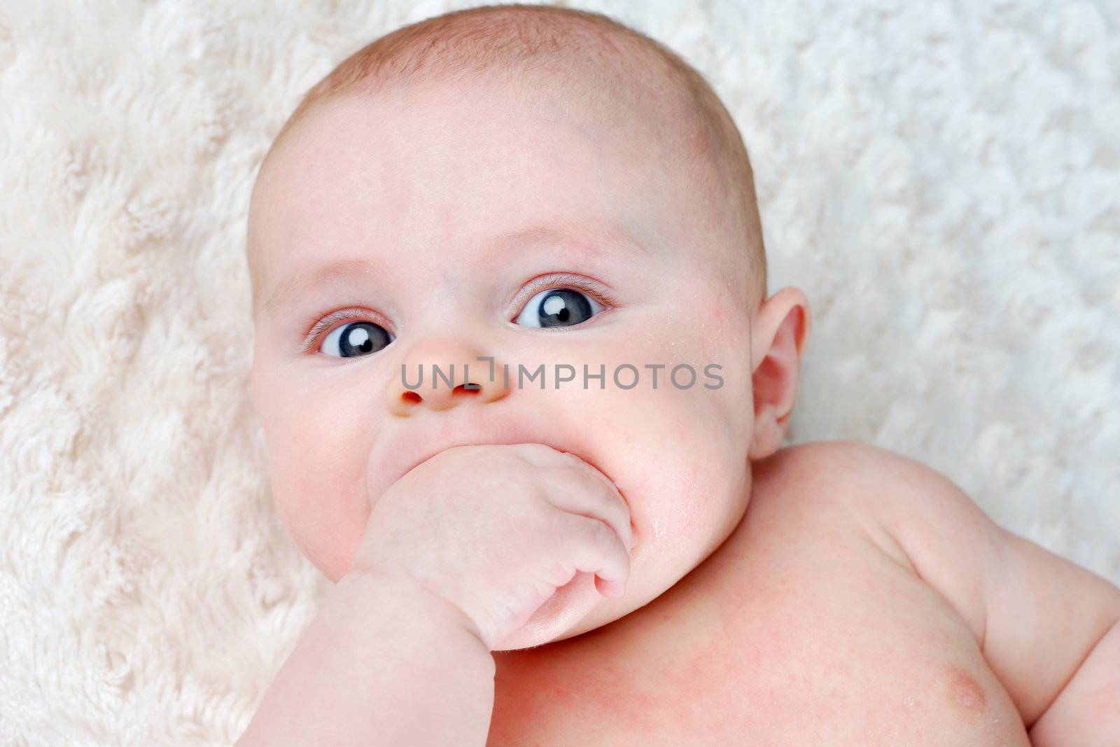 Portrait of beautiful 3 months old baby teething and sucking on its hand to sooth itself