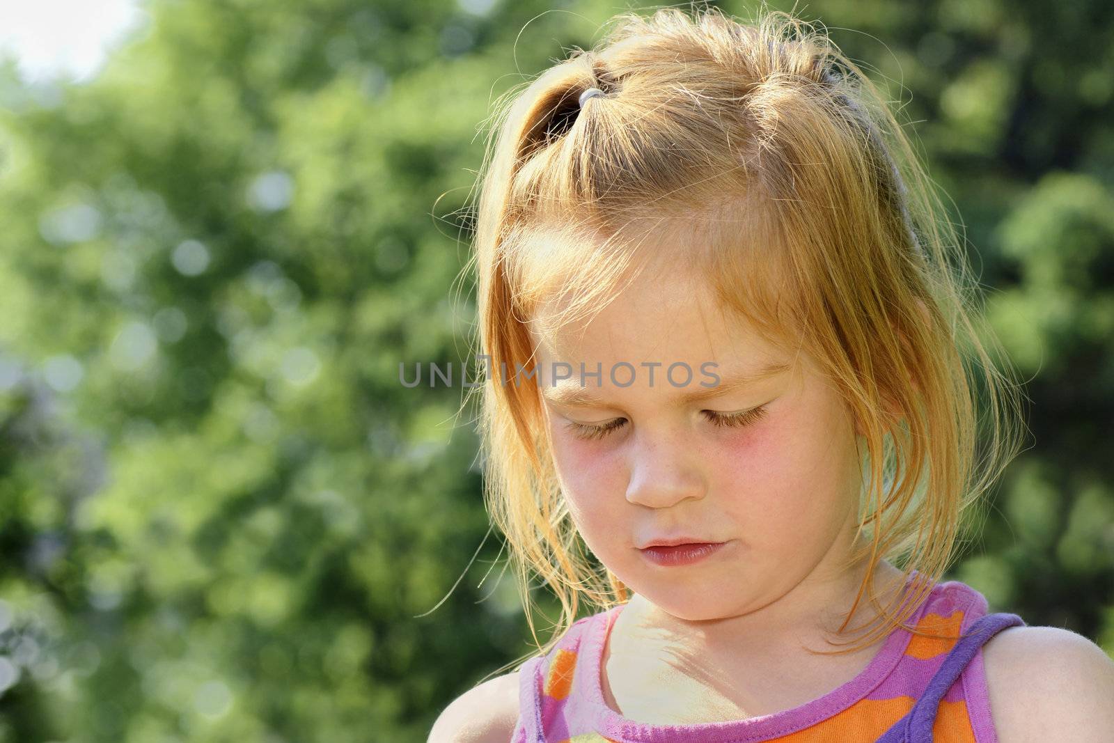 Sad or crying red haired little girl looking down.