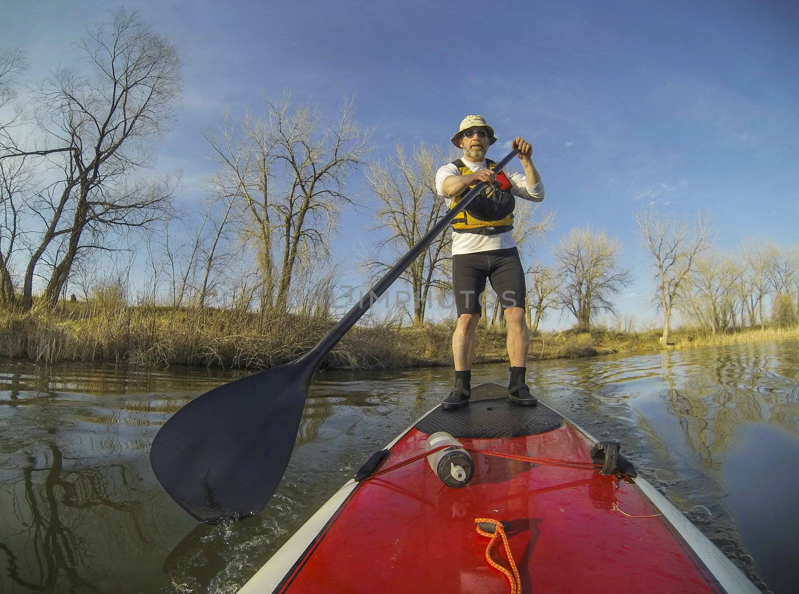 mature male paddler on a red stand up paddleboard (SUP), calm lake in Colorado, early spring
