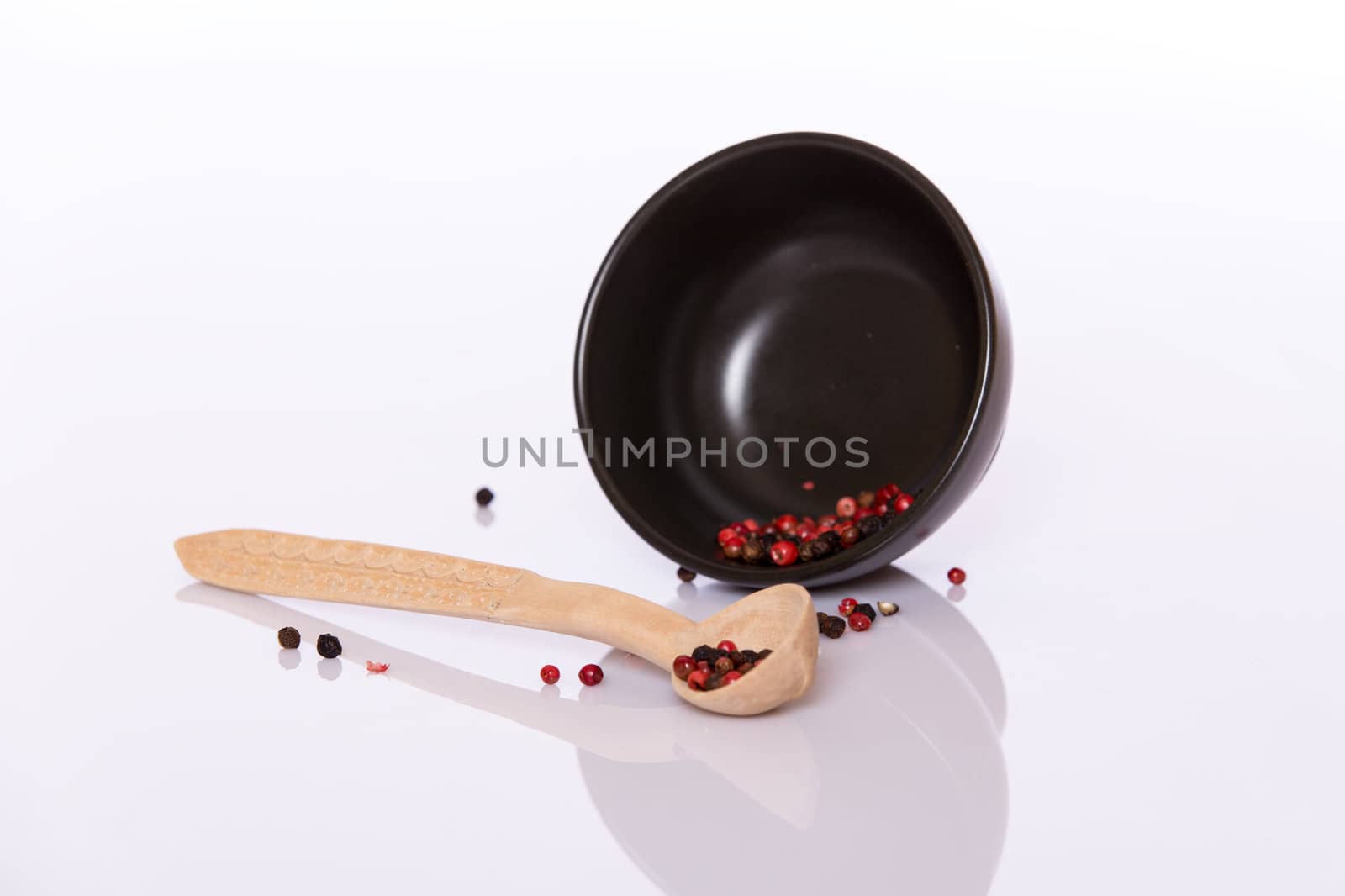 Black and rose pepper in wooden spoon and in black bowl