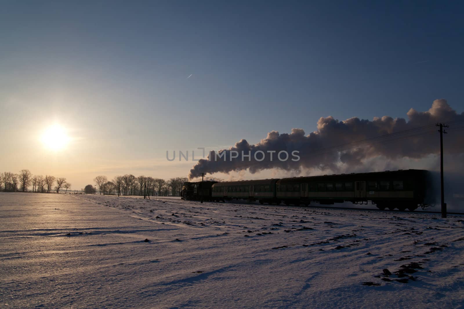 Vintage steam train puffing through countryside during wintertime
