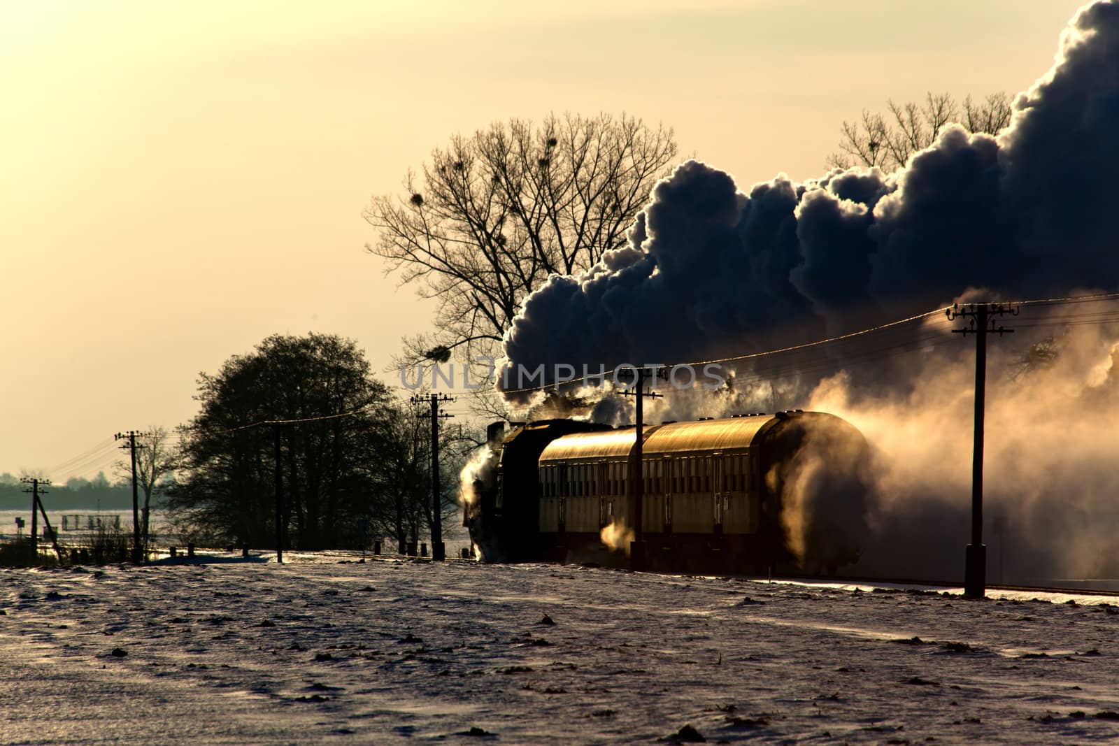 Vintage steam train puffing through countryside during wintertime
