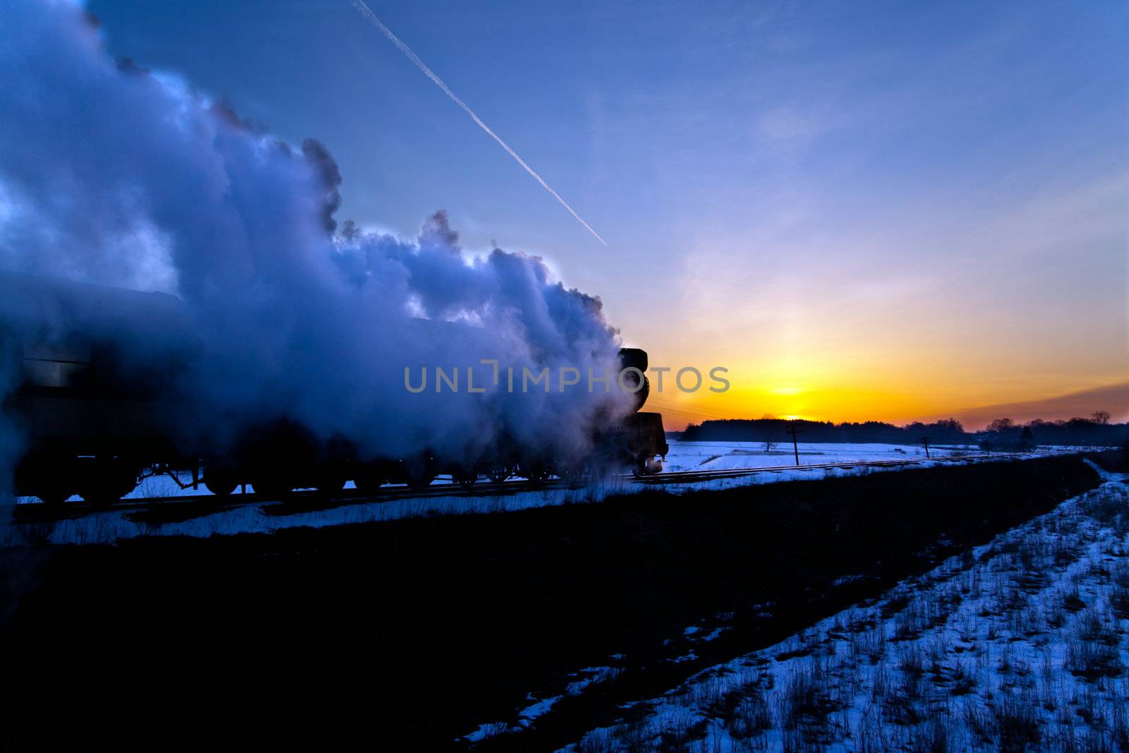 Vintage steam train puffing through countryside during wintertime
