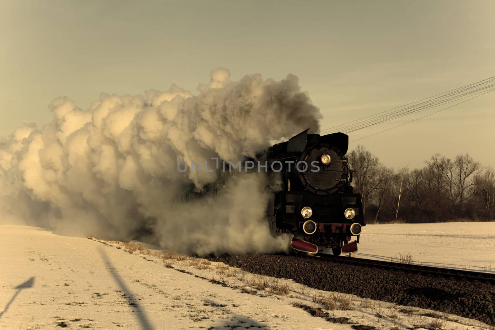 Vintage steam train puffing through countryside during wintertime
