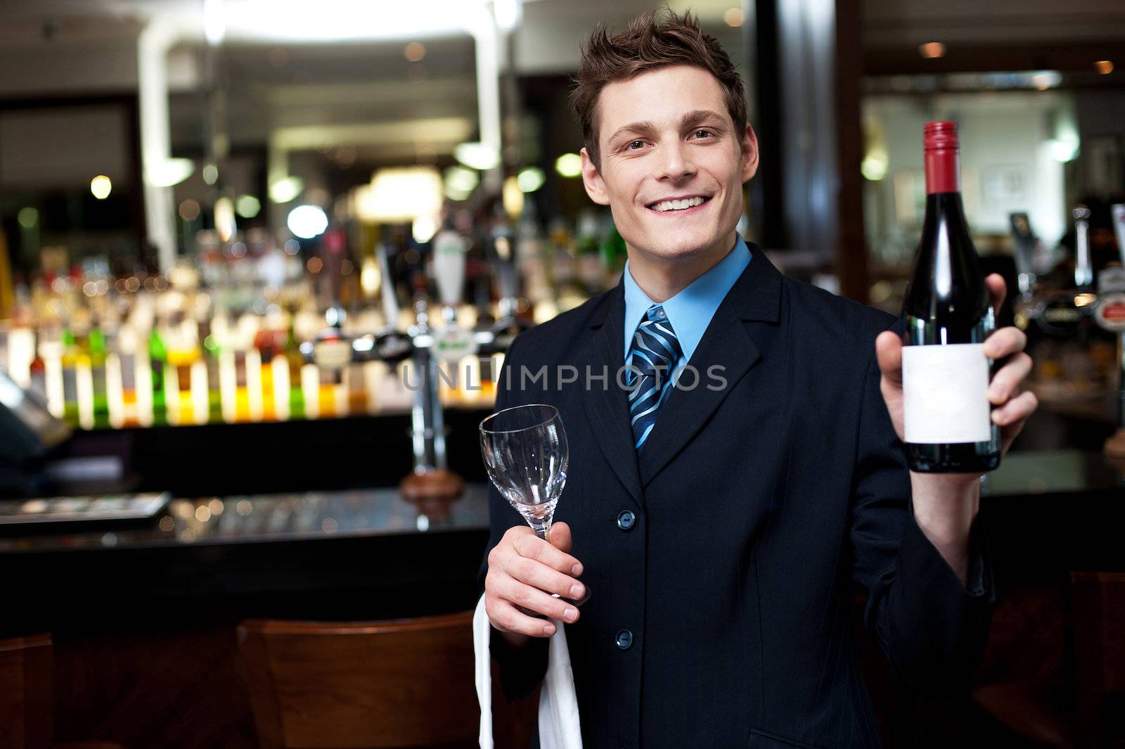 Cheerful executive posing with a bottle of wine. Bar in the background