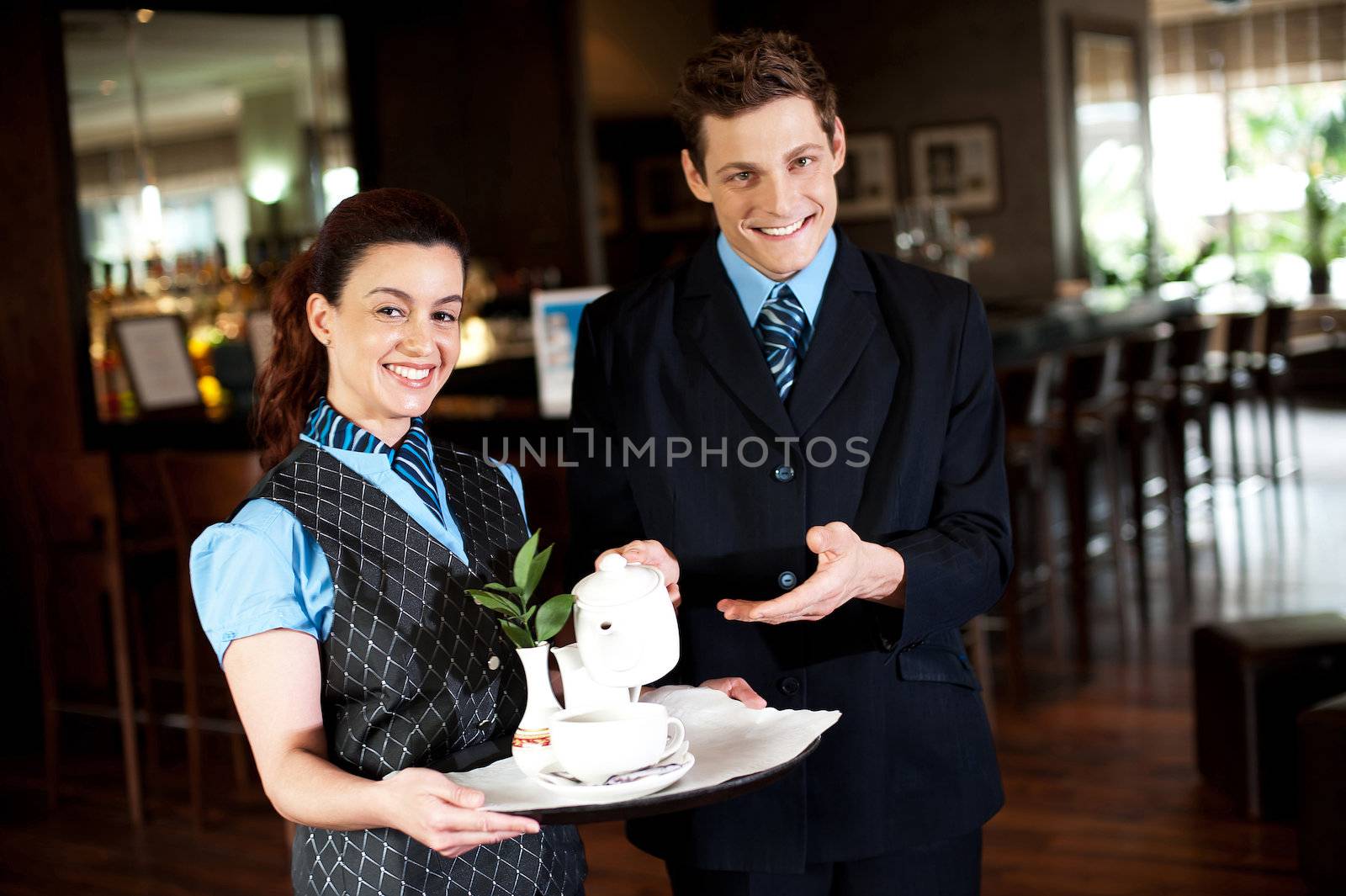 Here is cup of refreshing tea you ordered. Waitress holding tea tray as man pours