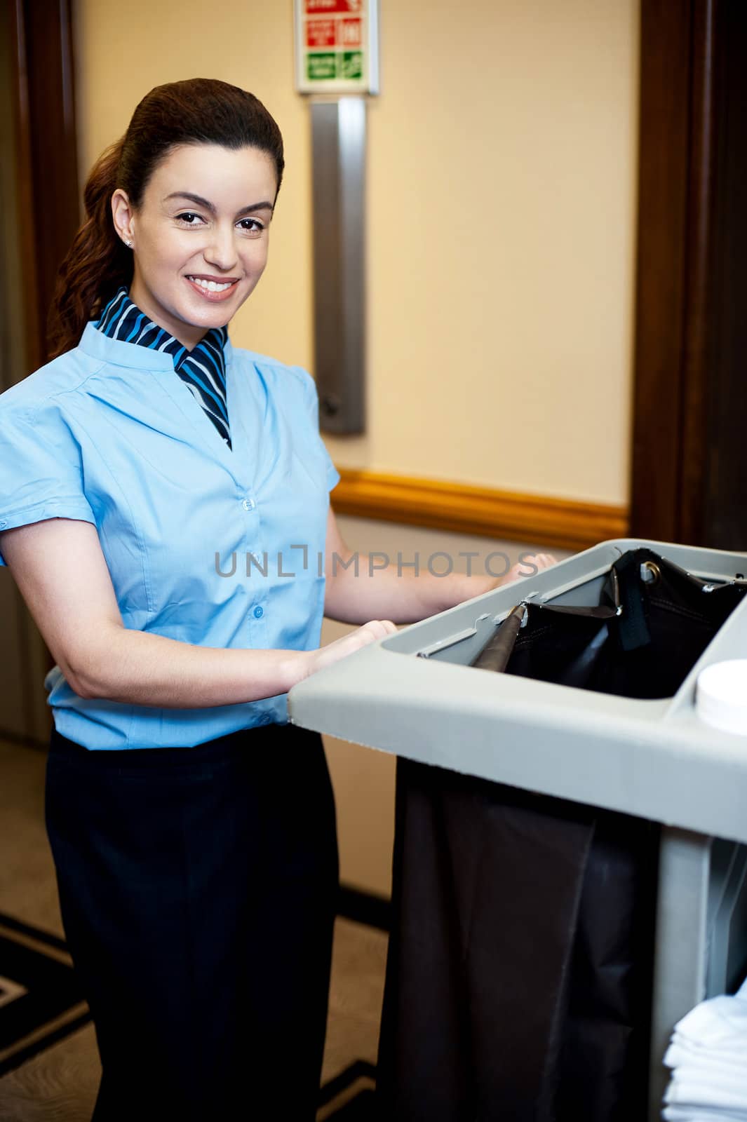 Female attendant posing with cart in hotel corridor