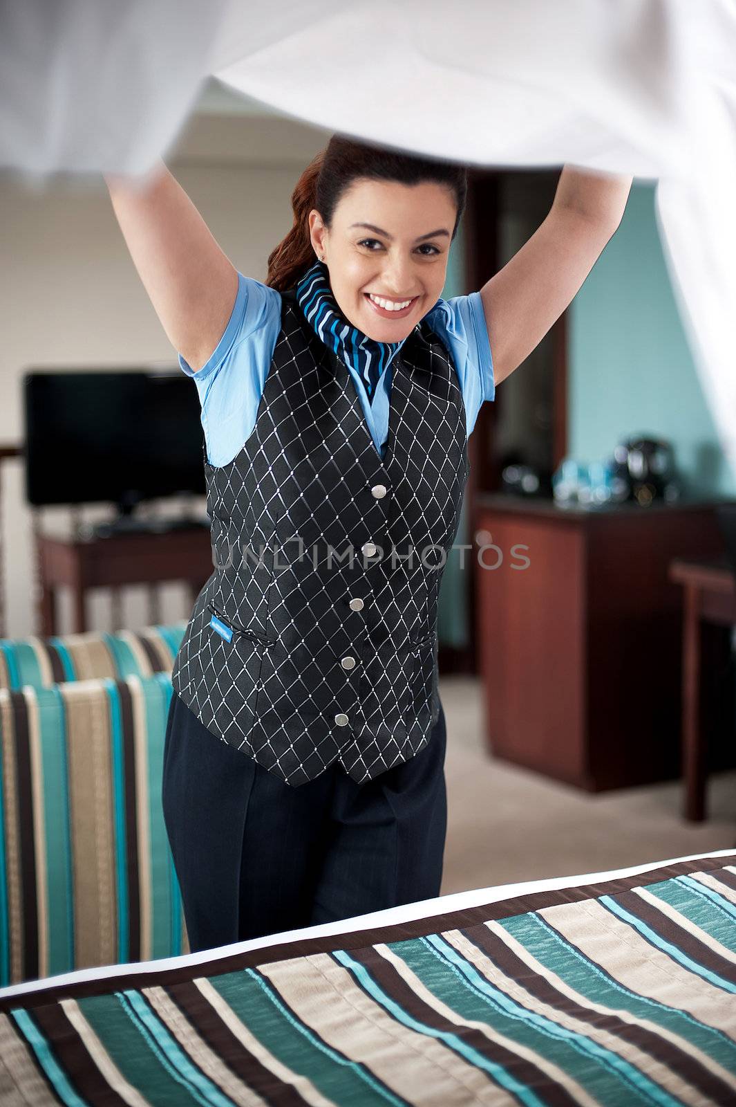 Charming female housekeeper replacing the sheets. Led tv in the background