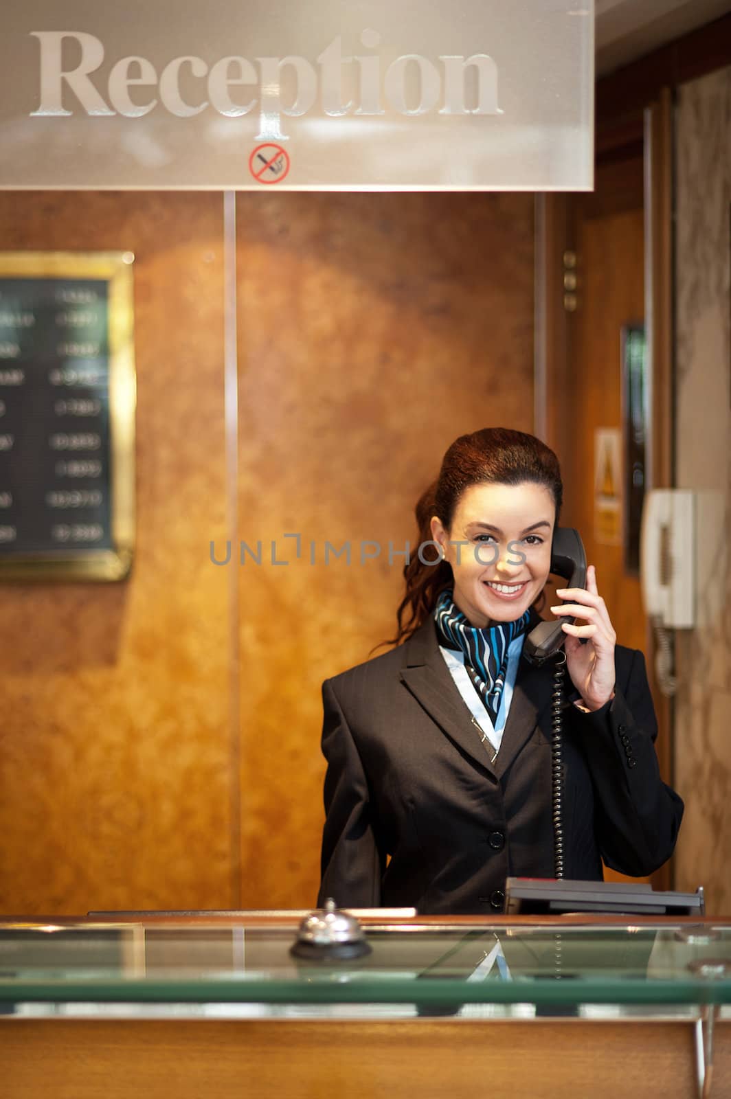 Attractive young receptionist in formal attire receiving calls and greeting customers with a smile