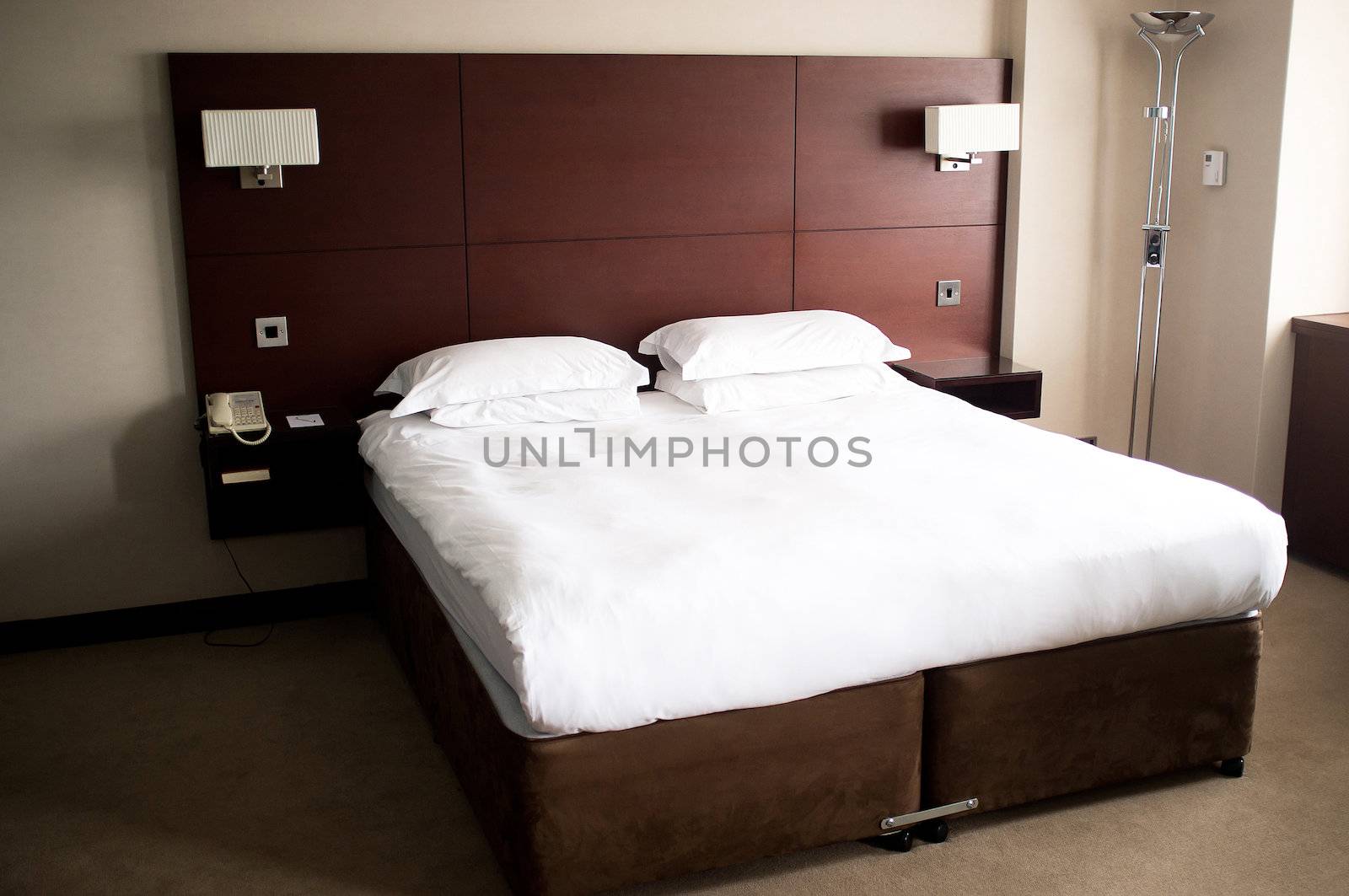 King sized bed in a suite with crisp white sheets on it and a headboard