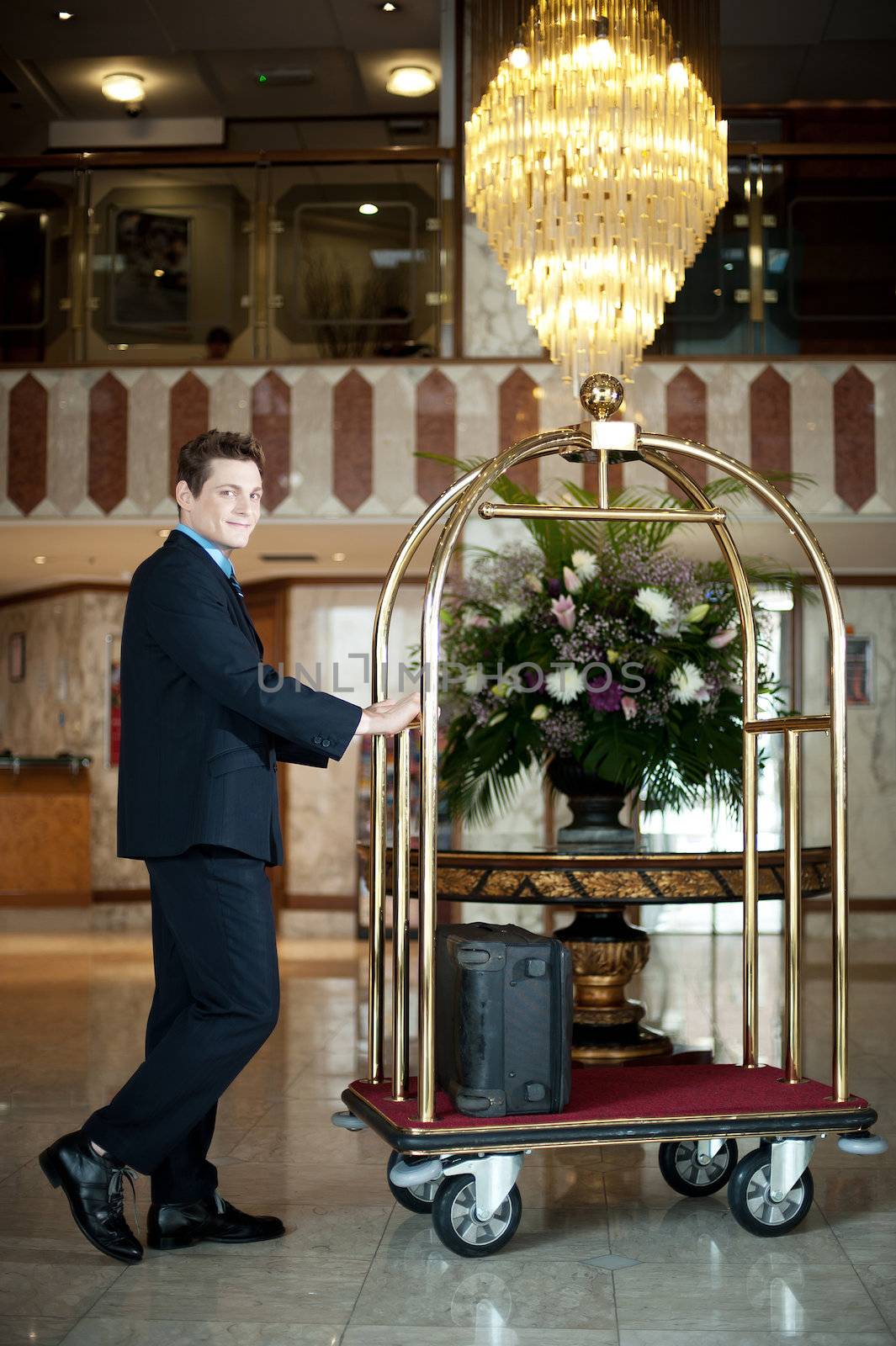 Handsome concierge pushing the luggage cart. Posing near master centerpiece